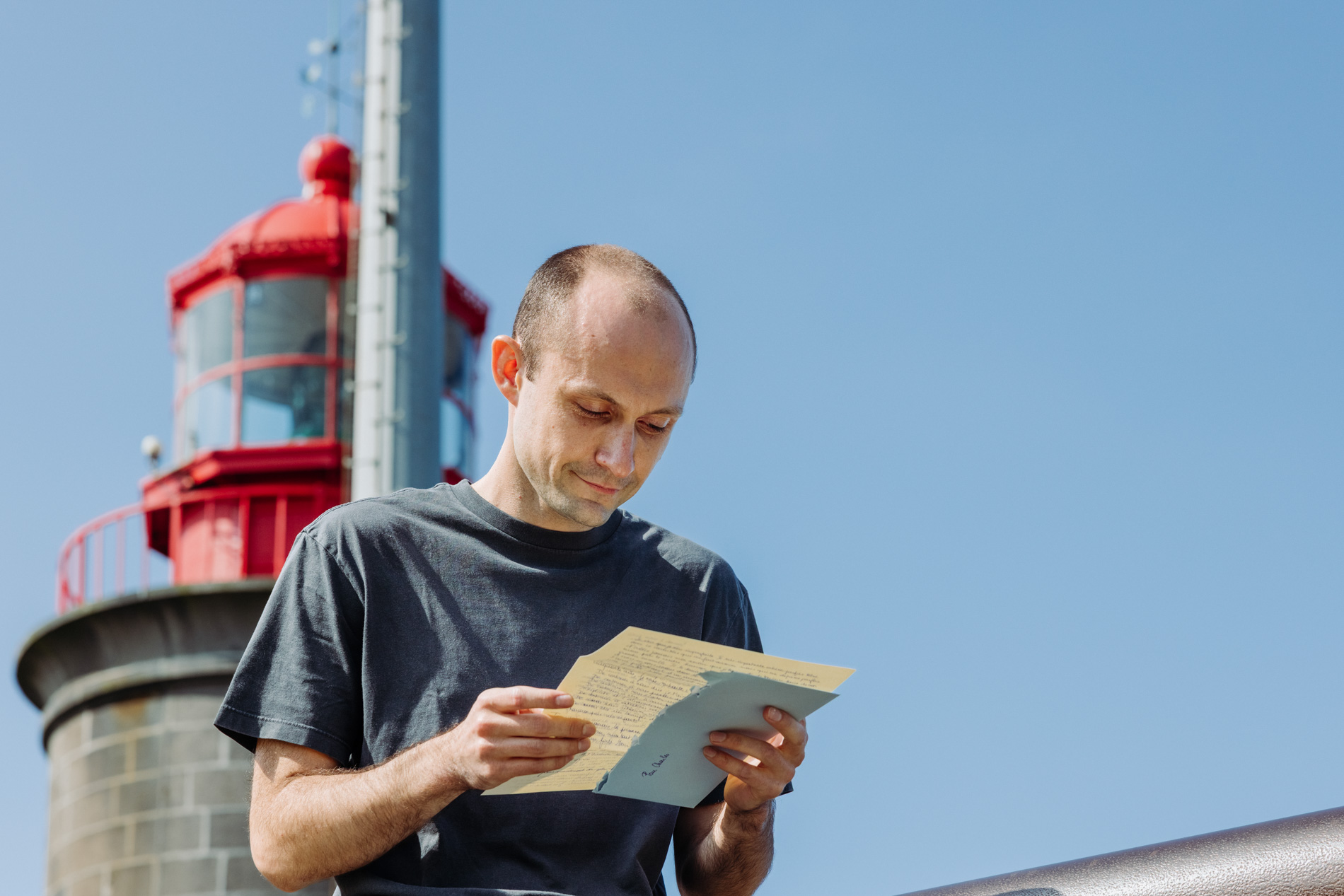 Un homme lisant une lettre avec un phare derrière