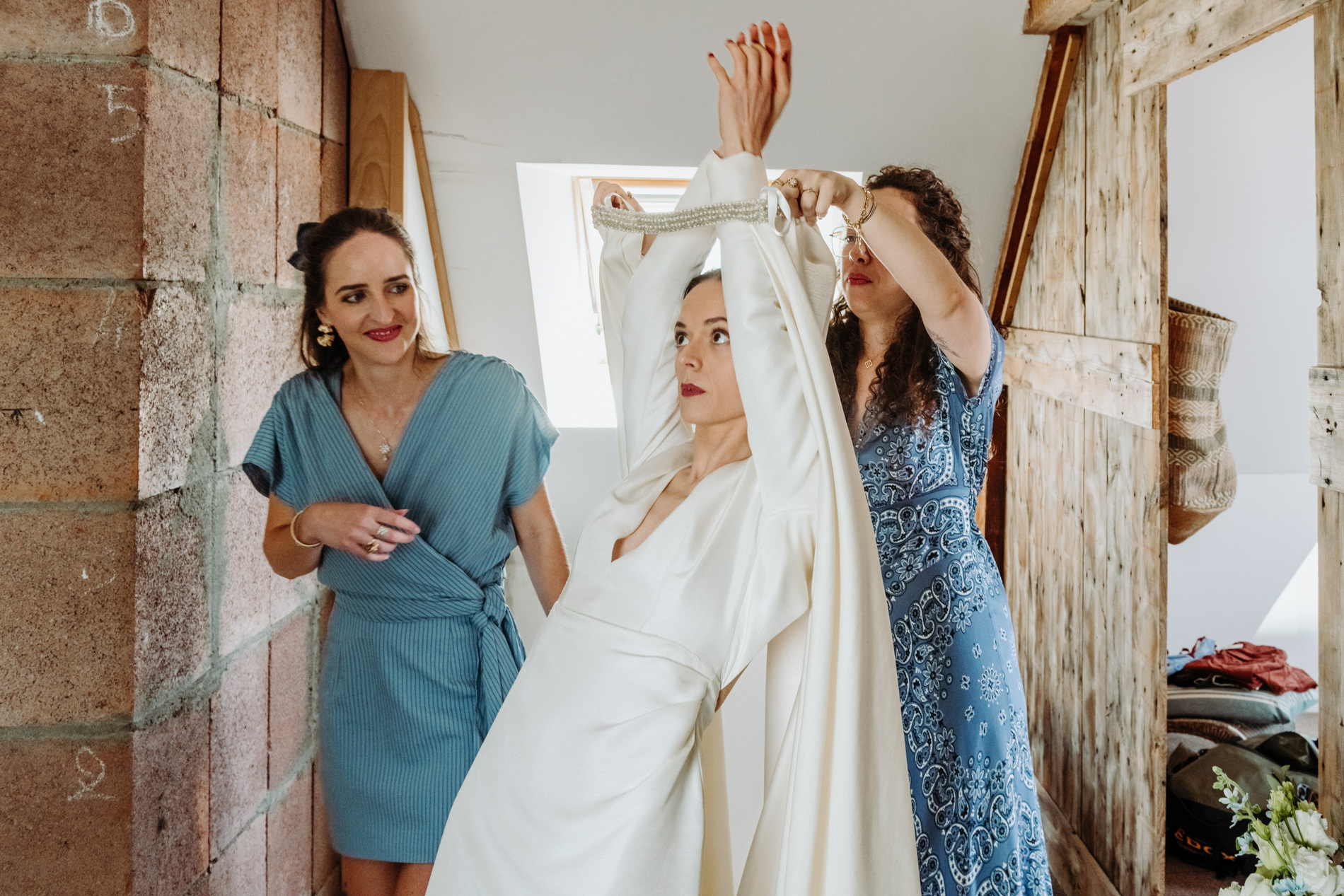 La mariée qui enfile sa robe aidée par deux femmes