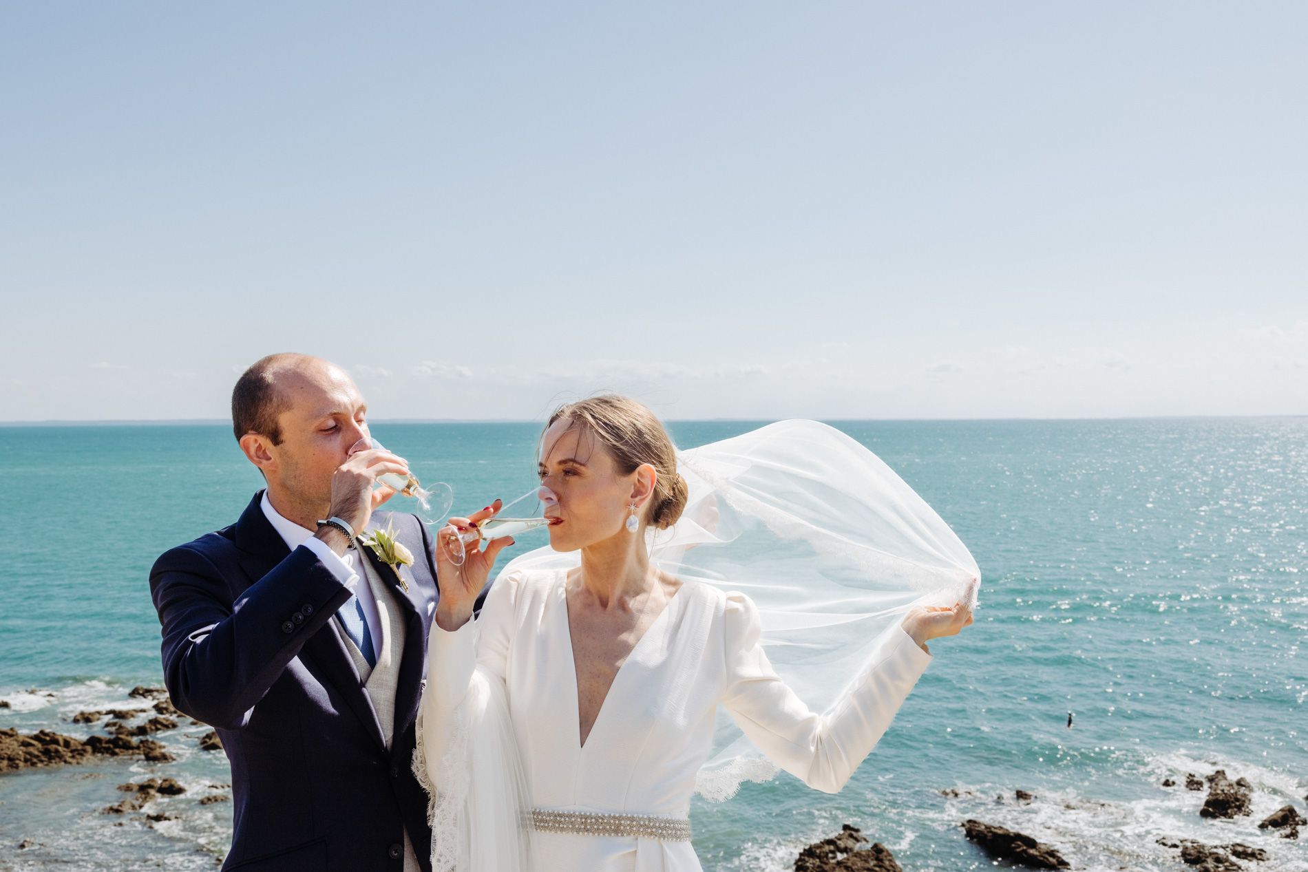 Couple de mariés buvant du champagne devant l'océan